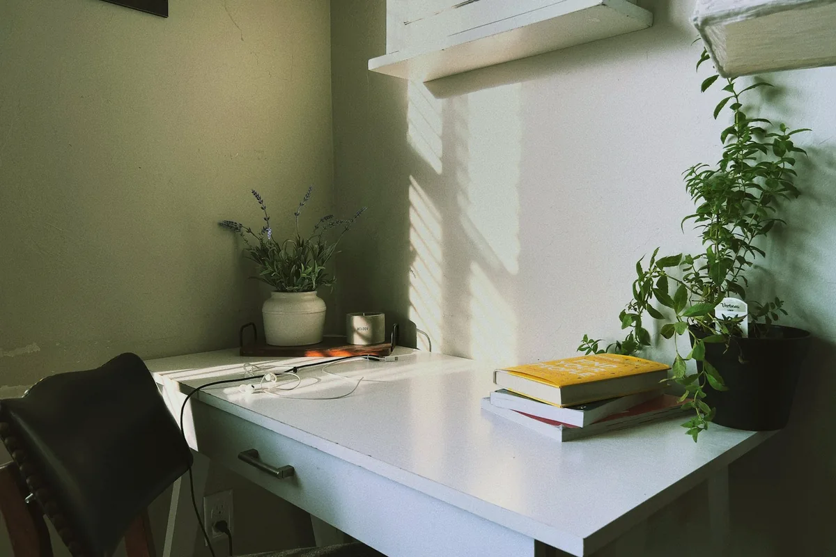 Bureau blanc près d’une fenêtre, plante verte et livres sous une lumière douce