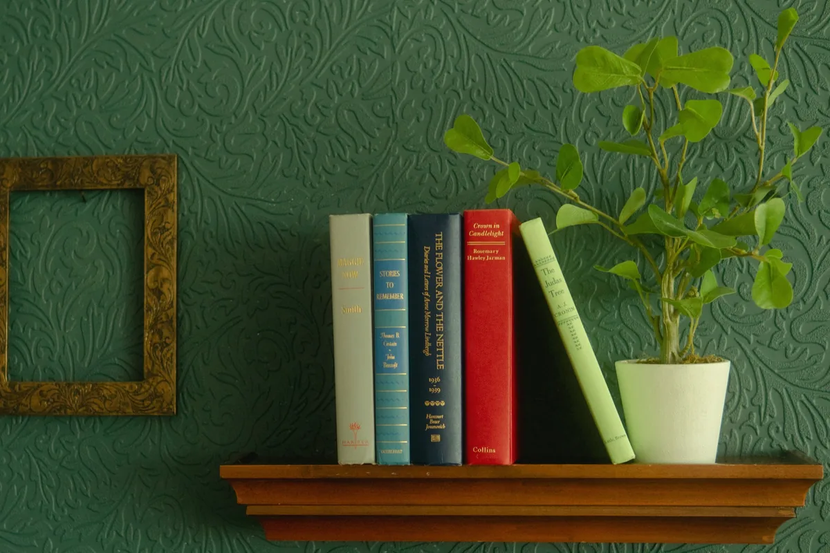 Étagère murale vert profond avec livres, cadre doré et plante