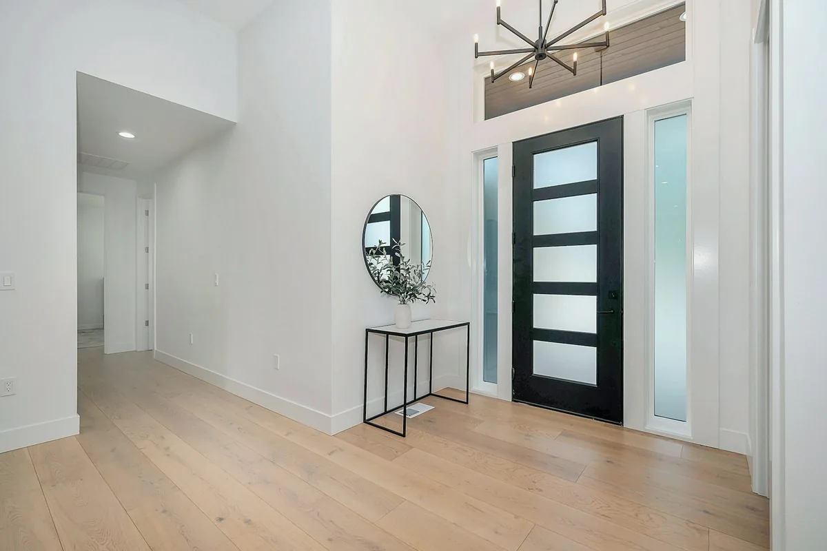 Hall lumineux avec porte vitrée et miroir rond sur un meuble d’entrée