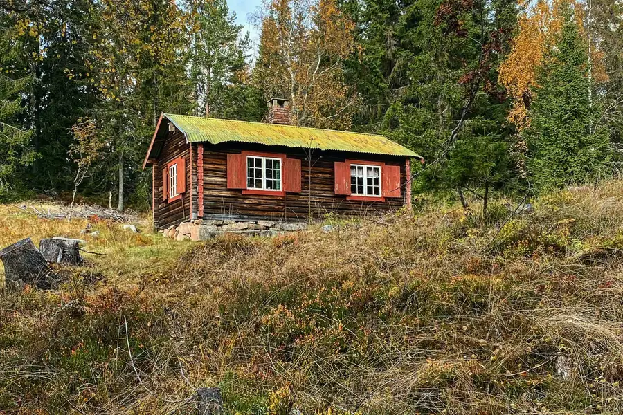 Petite maison en bois rouge au milieu d’une lande, sous un ciel clair